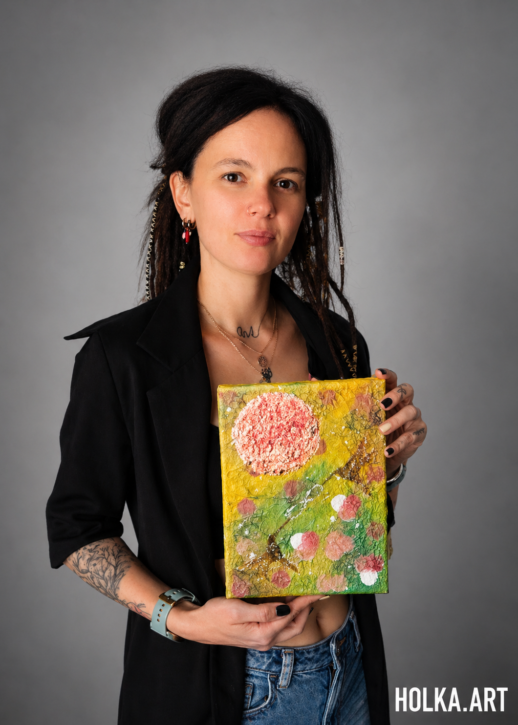 Portrait of a woman holding a colorful square artwork with pink circle and floral details against gray background.